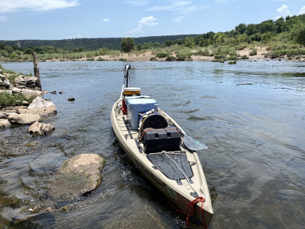 An kayak outfitted for fishing sits on the bank of a river.